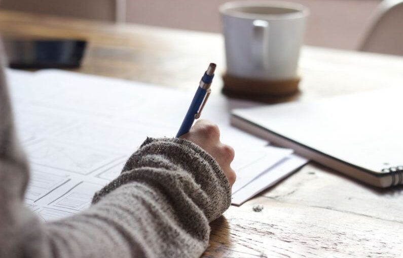 Mentorship Story - person writing on brown wooden table near white ceramic mug