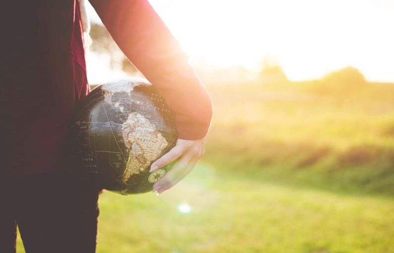 Global Citizenship - person holding black and brown globe ball while standing on grass land golden hour photography
