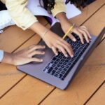 E-learning Platform - Crop ethnic schoolchildren typing on laptop while studying on street