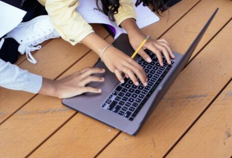 E-learning Platform - Crop ethnic schoolchildren typing on laptop while studying on street