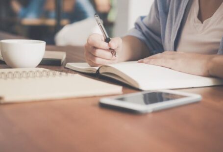 Mobile Learning - Woman Writing on a Notebook Beside Teacup and Tablet Computer