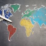 Global Classroom - Top view of crop anonymous person holding toy airplane on colorful world map drawn on chalkboard