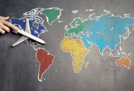 Global Classroom - Top view of crop anonymous person holding toy airplane on colorful world map drawn on chalkboard