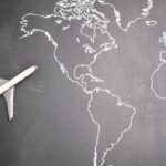 Globalization Education - Top view of miniature airplane placed on over gray world map with crop hand of anonymous person indicating direction representing travel concept