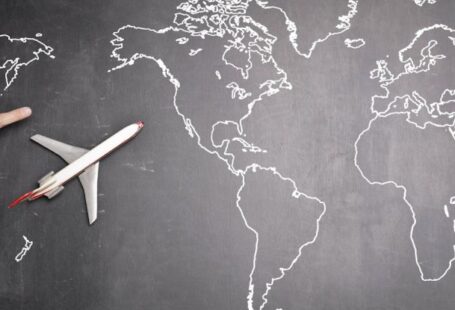 Globalization Education - Top view of miniature airplane placed on over gray world map with crop hand of anonymous person indicating direction representing travel concept