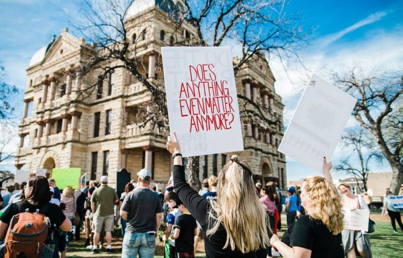 Student Activism - woman holding does anything even matter anymore? signage near building at daytime